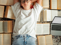 Cute teen girl student in casual clothing and glasses lying on books, back to school, exam preparation, top view