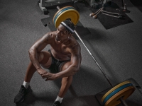 Stylish muscular athletic african american man sitting on floor with barbell in gym. Strength training concept. Top view