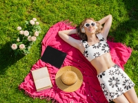 Pretty young illustrator blogger girl in sunglasses with tablet is lying on a green lawn, colorful photo for blog or ad