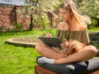 A happy and cute teen girl draws sketches on a tablet while sitting in the yard with a dog, in the garden, on the lawn.