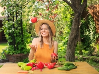 A young pretty girl in a hat is sitting at a wooden table with fresh vegetables grown in her garden in the summer.