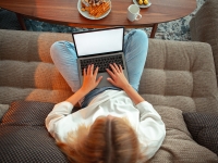 Teen girl sitting on sofa in Lotus position with blank screen laptop watching TV series with sweets and tea, top view